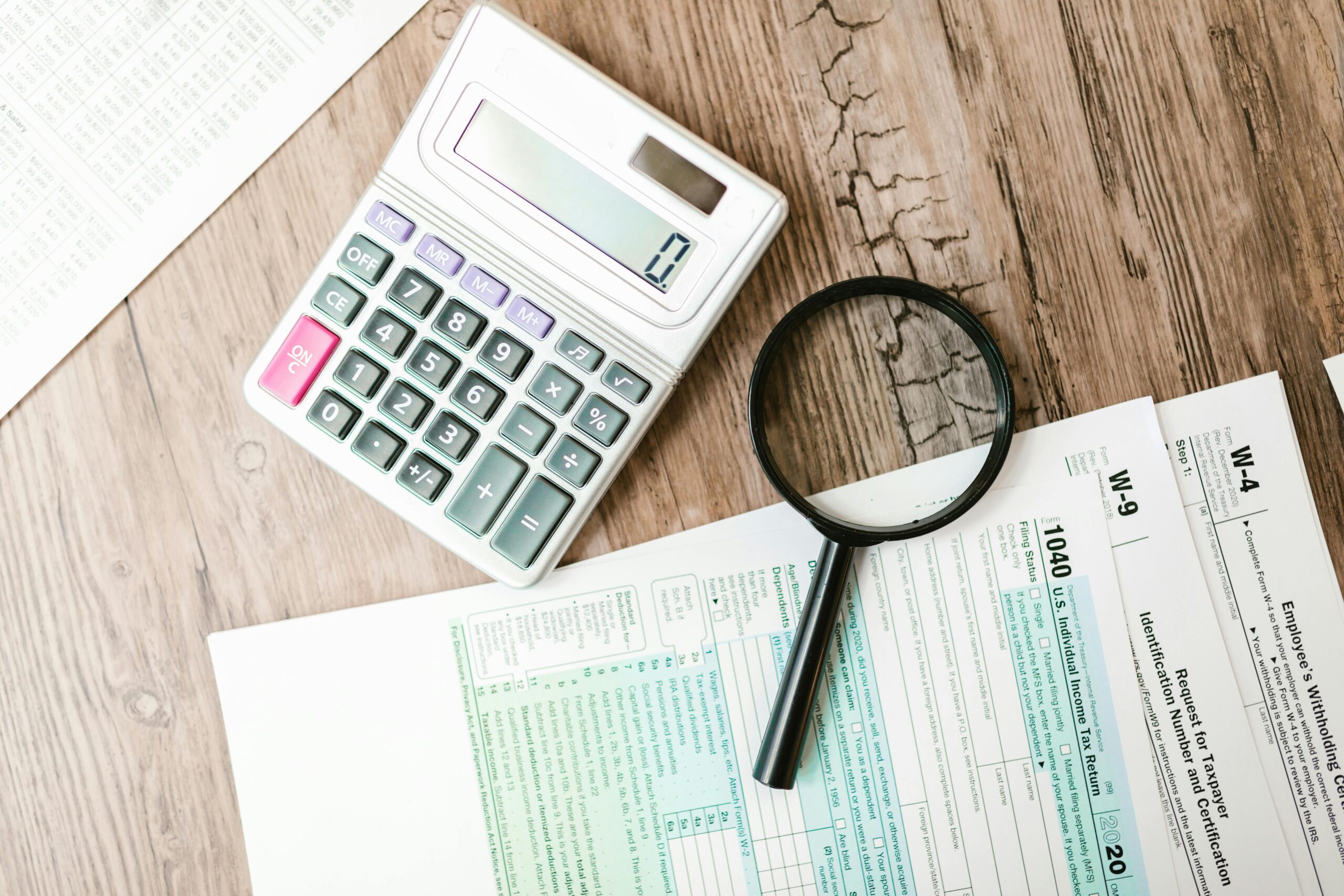 Tax forms laid out with a calculator and magnifying glass on a wooden surface, perfect for finance themes.